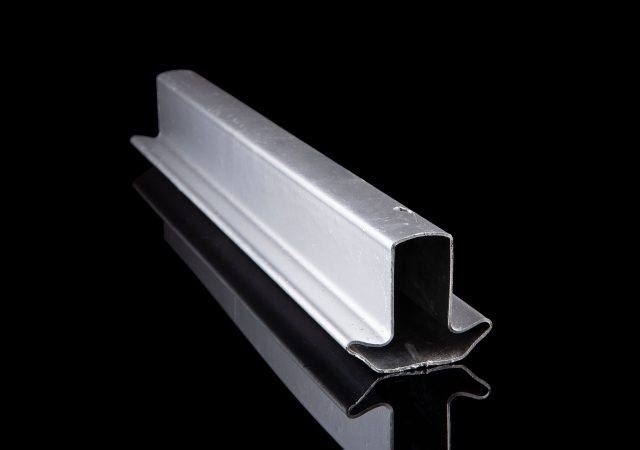 A metallic U-shaped channel rests diagonally on a reflective black surface, much like the sleek design of Clearview fencing, highlighting its industrial elegance and smooth texture.