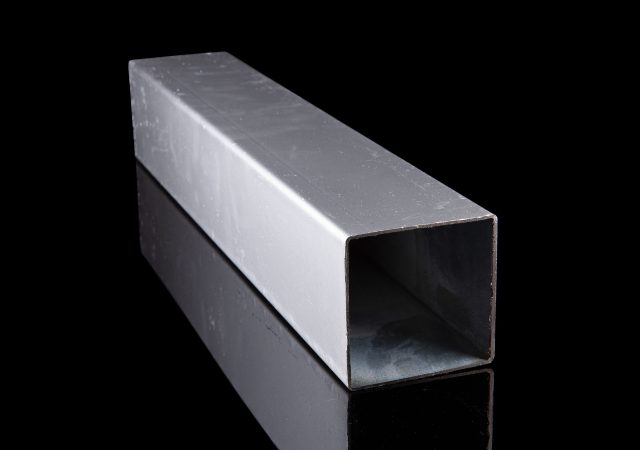 A long, rectangular metal box with an open end is placed on a reflective black surface, creating a mirror-like effect below it. The industrial design echoes that of clearview fencing, boasting a smooth and shiny surface.