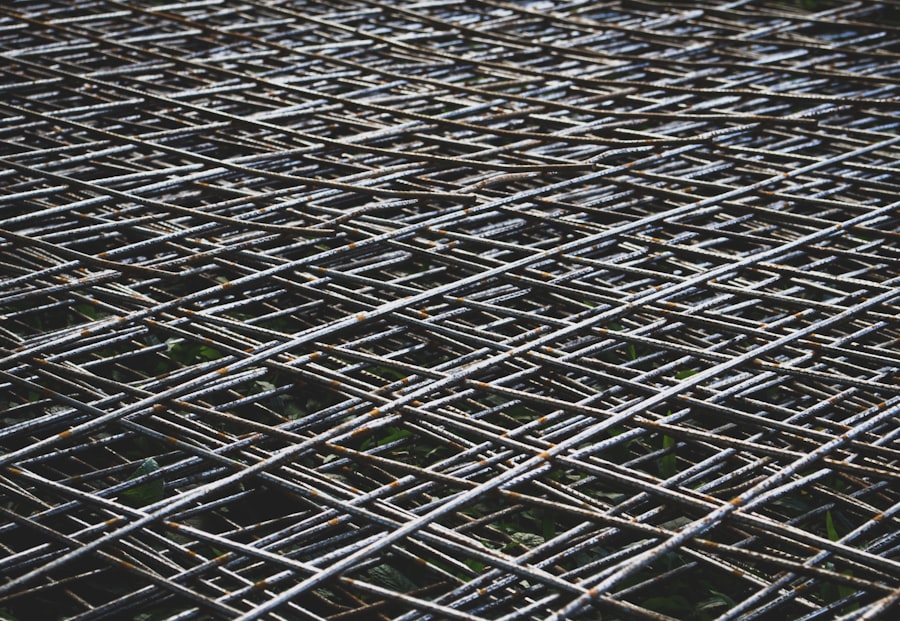 Close-up view of overlapping metal rods arranged in a dense, crisscrossed grid pattern, reminiscent of clear view fencing. The rods are weathered and have a metallic sheen, creating an abstract, geometric texture.